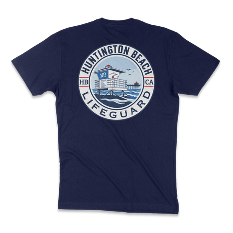 A navy blue short-sleeve t-shirt shown from the back, featuring a large circular graphic print on the center back. The graphic depicts a lifeguard tower over blue water with the text 'HUNTINGTON BEACH LIFGUARD' in white and blue, and 'HB CA' on the sides.