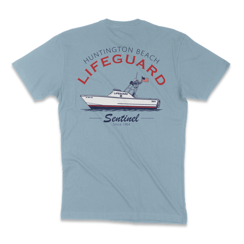 A light blue short-sleeve t-shirt shown from the back, featuring a graphic print of a 'Huntington Beach Lifeguard' boat on the back with red and black lettering.