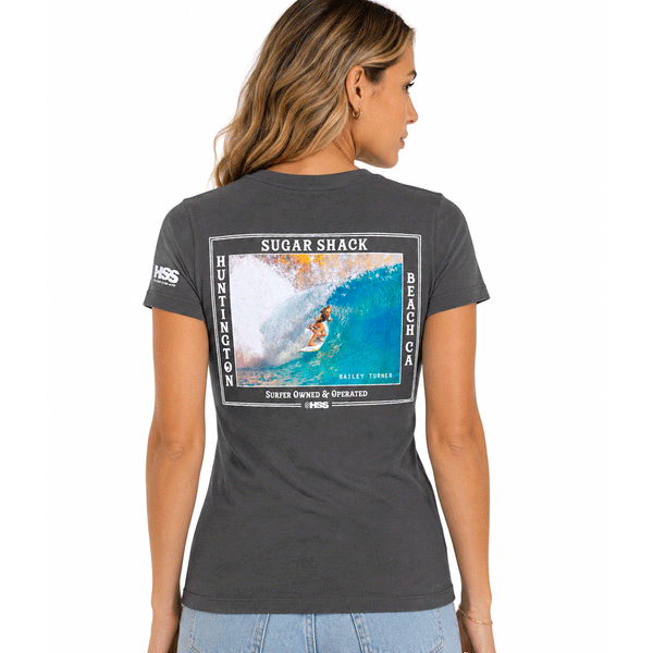 back of woman wearing grey t-shirt with the text Sugar Shack Huntington Beach and picture of Bailey Turner surfing
