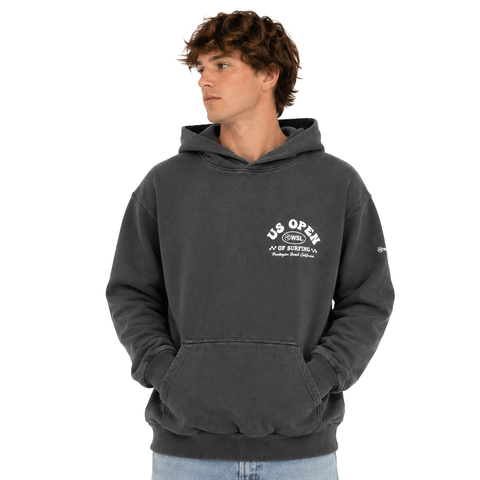 Front view of person wearing a charcoal heavyweight hooded sweatshirt featuring a white US Open of Surfing logo on the left chest. The pullover hoodie includes a kangaroo pocket, ribbed cuffs and waistband, and a vintage-washed finish, displayed on a clean white background.