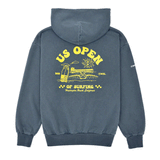 Back view of a indigo blue heavyweight hooded sweatshirt featuring a large yellow US Open of Surfing graphic with a surfboard, ocean waves, sun illustration, and Huntington Beach Pier artwork. The pullover hoodie has a vintage-washed finish, ribbed cuffs and waistband, and is displayed on a clean white background.