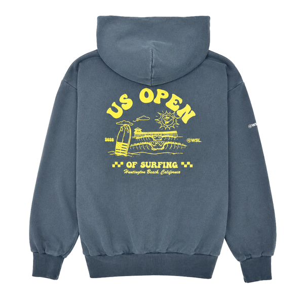 Back view of a indigo blue heavyweight hooded sweatshirt featuring a large yellow US Open of Surfing graphic with a surfboard, ocean waves, sun illustration, and Huntington Beach Pier artwork. The pullover hoodie has a vintage-washed finish, ribbed cuffs and waistband, and is displayed on a clean white background.