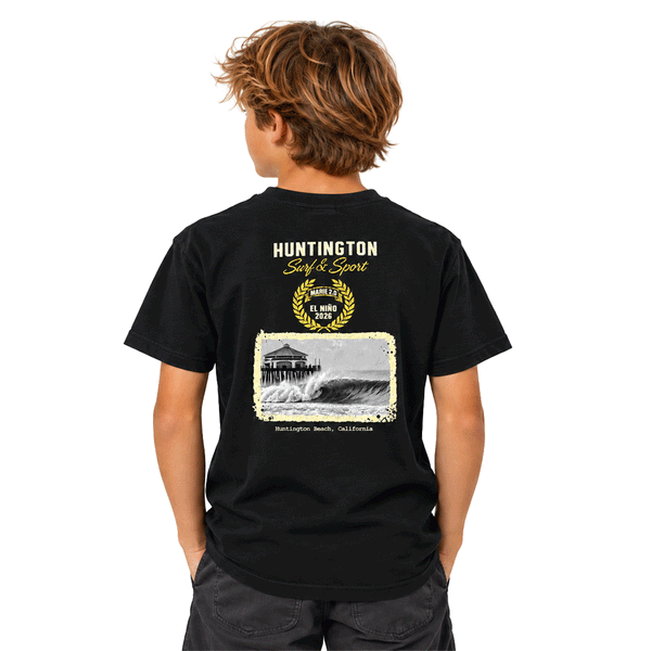 back of boy wearing black t-shirt with image of the HB PIer and a wave. above image reads Huntington Surf and Sport. El Nino 2026. 