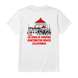 white US Open of Surfing t-shirt against a clean white background. The shirt features a back graphic of the Huntington Beach Pier with red rooftops and black linework above red text reading “US Open of Surfing Huntington Beach California.”