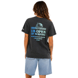 Back view of woman wearing a washed black US Open of Surfing T-shirt with blue graphic and light denim shorts on a white background.