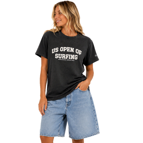 Woman wearing a washed black WSL US Open of Surfing boyfriend-fit T-shirt with white graphic on a white background.