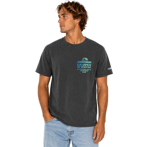 front view of person wearing a washed black-colored US Open of Surfing short-sleeve t-shirt displayed on a white background. The tee features a small multicolor retro-style surf graphic on the chest with "US Open of Surfing Huntington Beach California 2026" text and a WSL logo printed on the right sleeve.