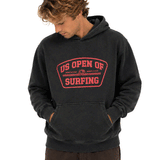 Man wearing a washed black US Open of Surfing pullover hoodie with red front graphic, looking down, on a white background.