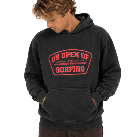 Man wearing a washed black US Open of Surfing pullover hoodie with red front graphic, looking down, on a white background.